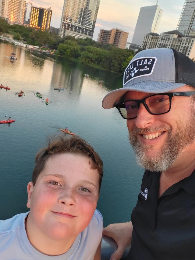Shane and Conor smiling together, a river and city skyline behind them