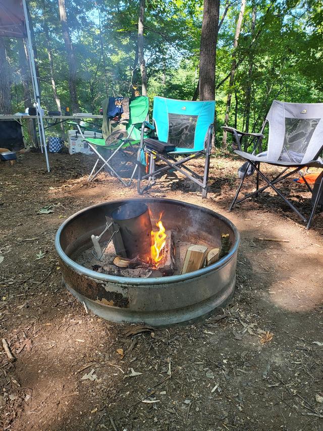 A campfire burning low in a steel fire ring at a wooded campsite